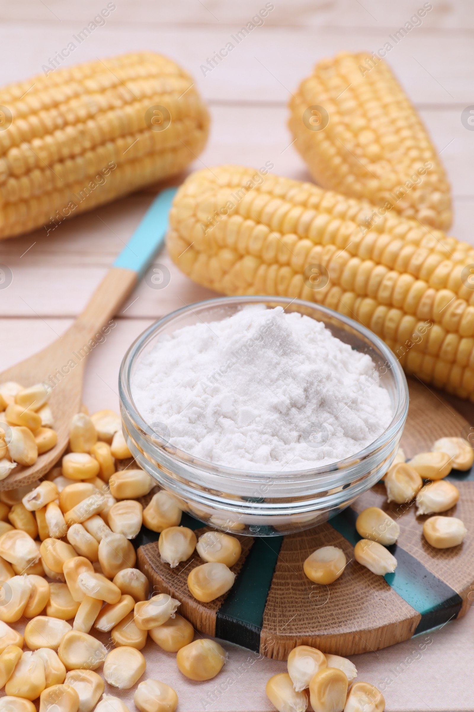 Photo of Bowl with corn starch, ripe cobs and kernels on wooden table