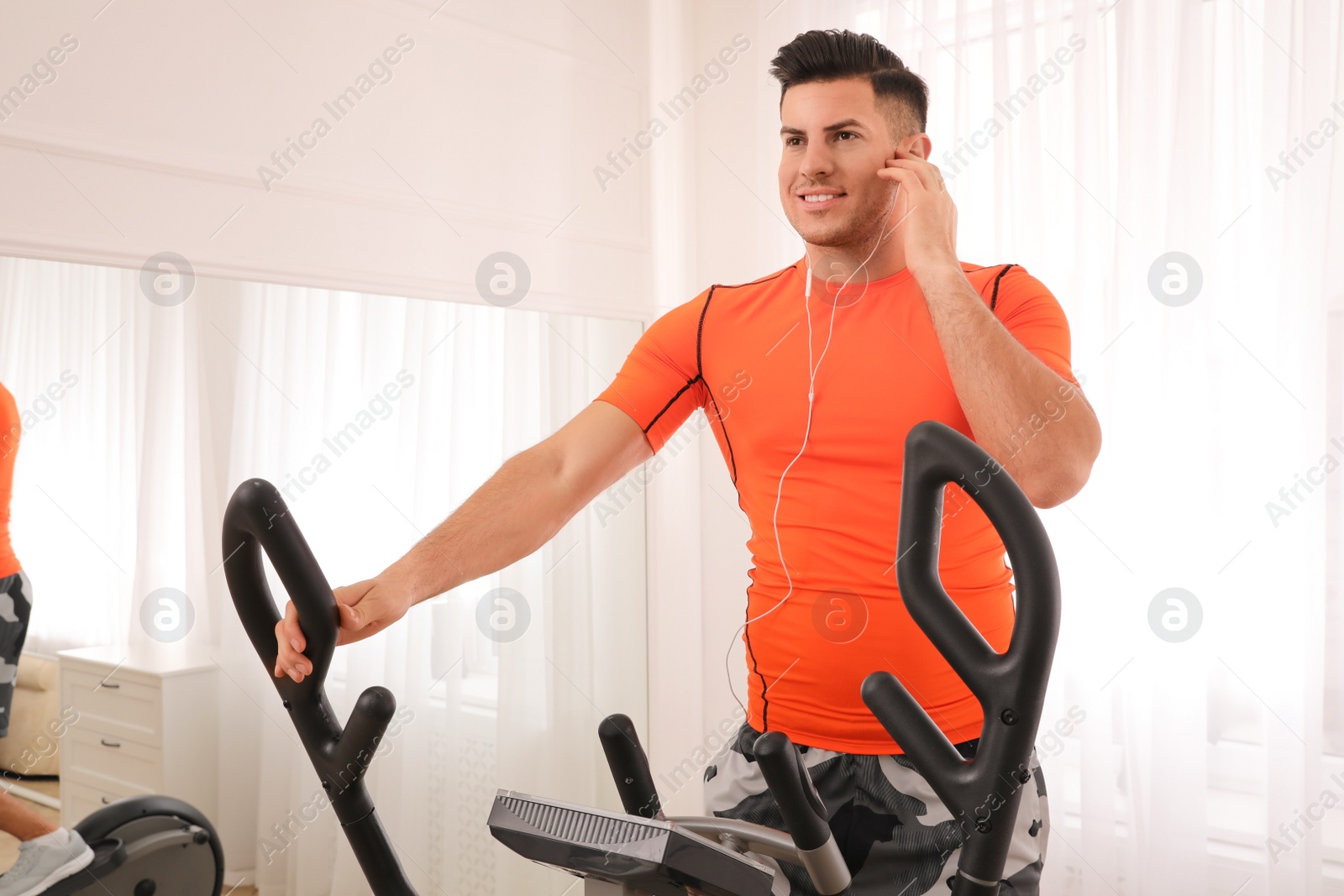 Photo of Man using modern elliptical machine at home