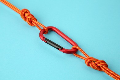 Photo of One metal carabiner with ropes on light blue background, closeup
