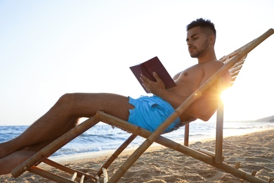 Young man reading book on sandy beach near sea