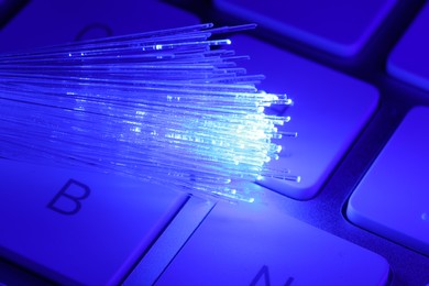 Photo of Optical fiber strands transmitting blue light on computer keyboard, macro view