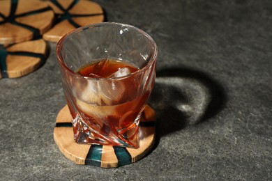 Glass of cold drink and stylish wooden cup coaster on grey table, space for text