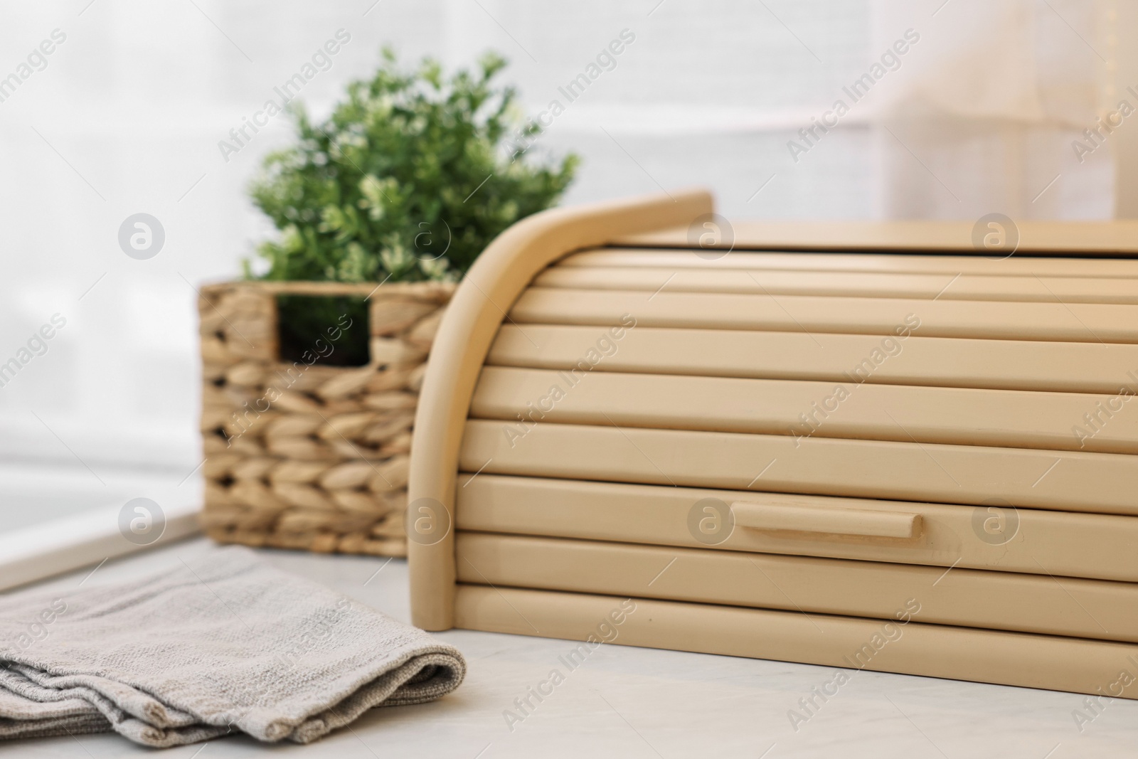 Photo of Wooden bread box and houseplant on white marble countertop in kitchen, closeup