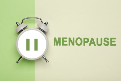 Menopause word and alarm clock with pause symbol on color background, top view