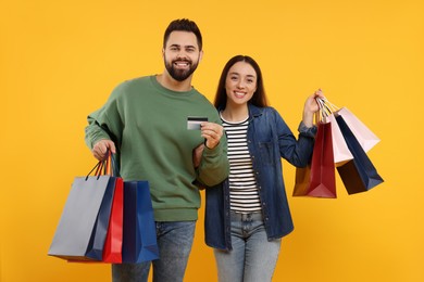 Photo of Happy couple with shopping bags and credit card on orange background