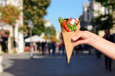 Photo of Woman holding wafer with falafel and vegetables outdoors, closeup. Space for text