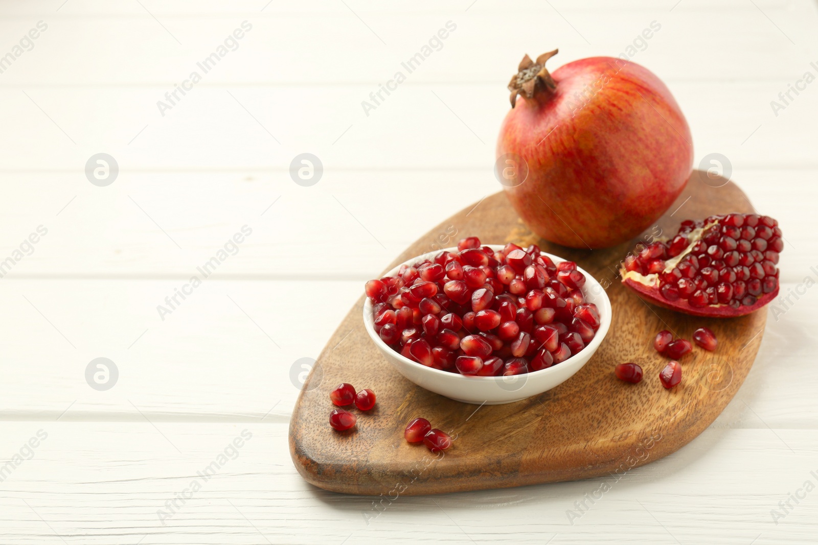 Photo of Ripe juicy pomegranate with grains on white wooden table. Space for text