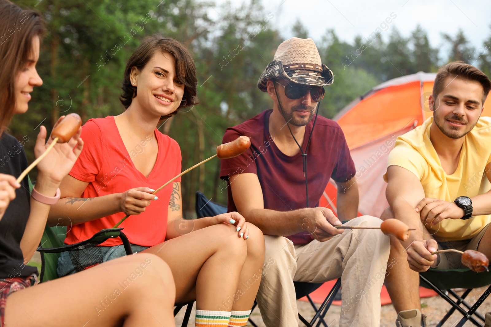 Photo of People having lunch with sausages near camping tent outdoors