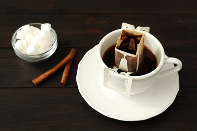 Photo of Cup with drip coffee bag, sugar and cinnamon on brown wooden table