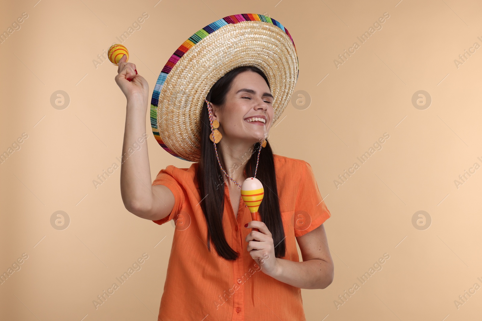 Photo of Young woman in Mexican sombrero hat dancing with maracas on beige background