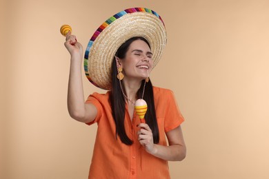 Photo of Young woman in Mexican sombrero hat dancing with maracas on beige background