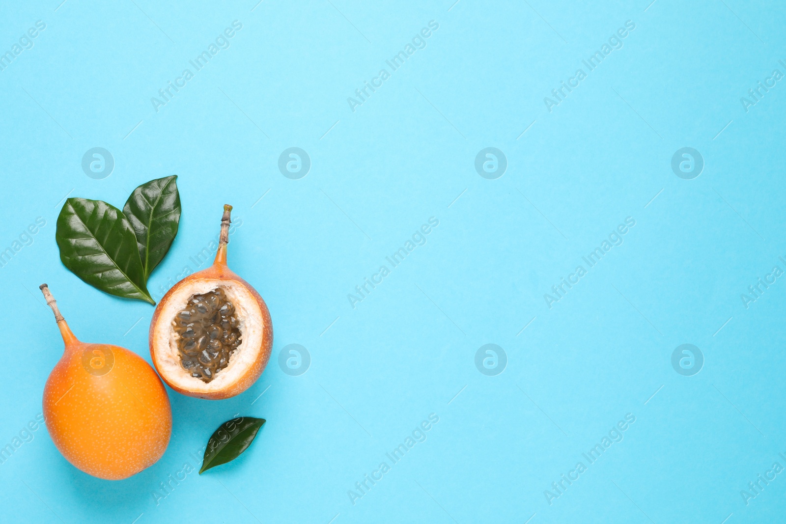 Photo of Delicious ripe granadillas with leaves on light blue background, flat lay. Space for text