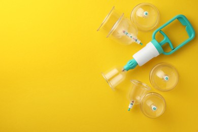 Photo of Plastic cups and hand pump on yellow background, flat lay with space for text. Cupping therapy