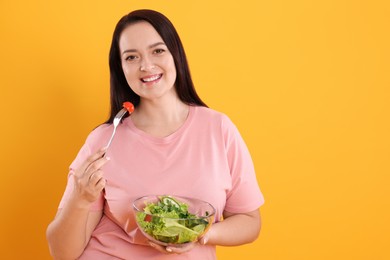 Photo of Beautiful overweight woman eating salad on yellow background, space for text. Healthy diet