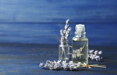 Bottle of natural essential oil and lavender flowers on blue wooden background. Space for text