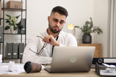 Photo of Overwhelmed man sitting at table with laptop and documents in office