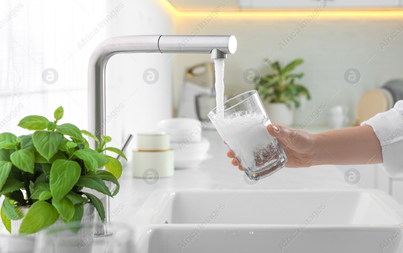 Photo of Woman filling glass with water from tap in kitchen, closeup