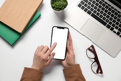 Woman using smartphone at white table, top view