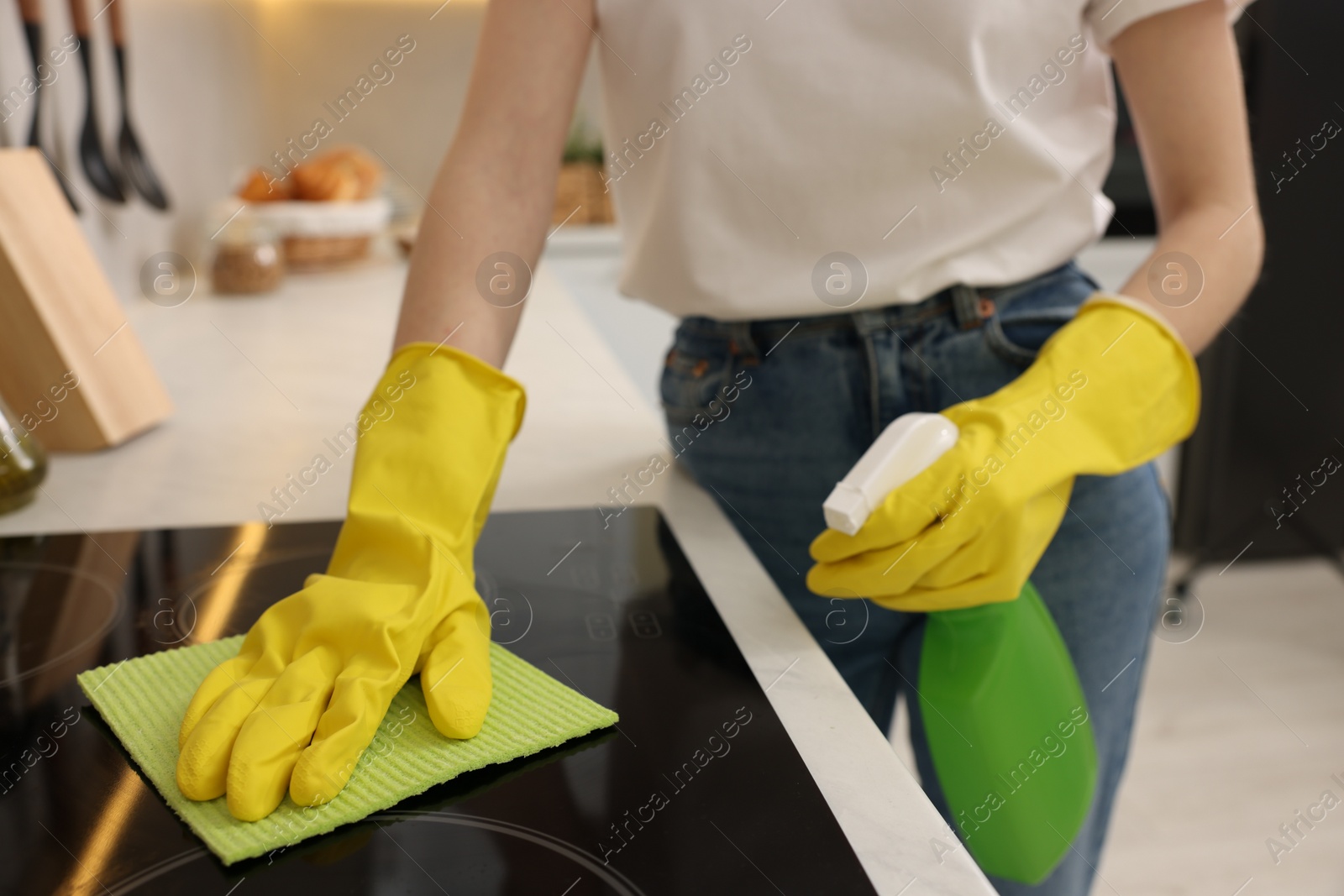 Photo of Woman with spray bottle and microfiber cloth cleaning electric stove in kitchen, closeup