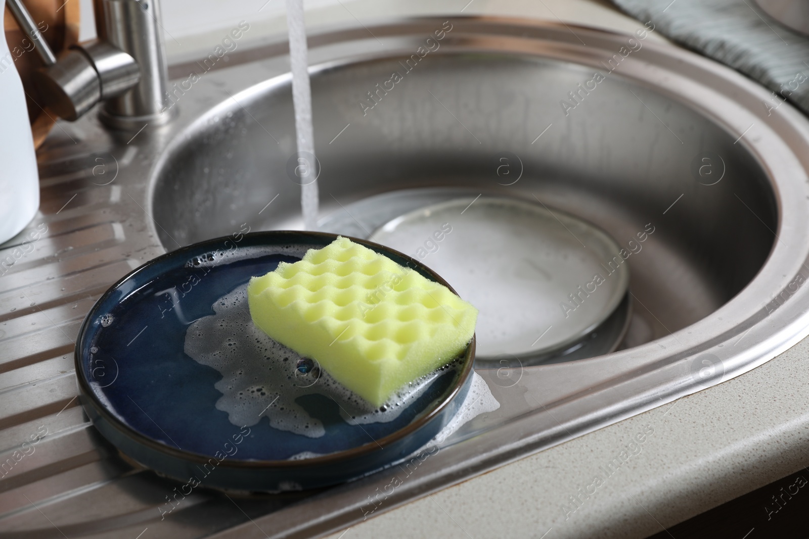 Photo of Plates and sponge in kitchen sink. Washing dishes