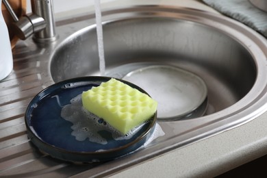 Photo of Plates and sponge in kitchen sink. Washing dishes