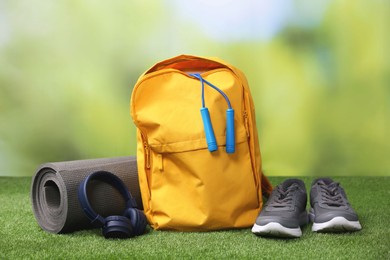 Photo of Backpack and different sports equipment on grass against blurred background