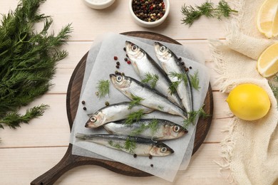 Photo of Fresh raw sprats, lemon, dill and peppercorns on light wooden table, flat lay