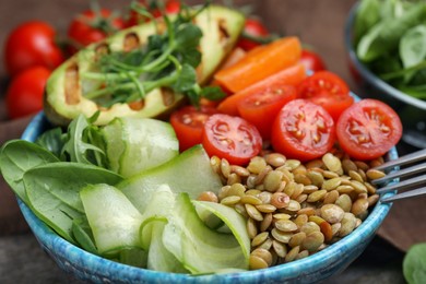 Delicious lentil bowl with avocado, tomatoes, carrot and cucumber on table, closeup