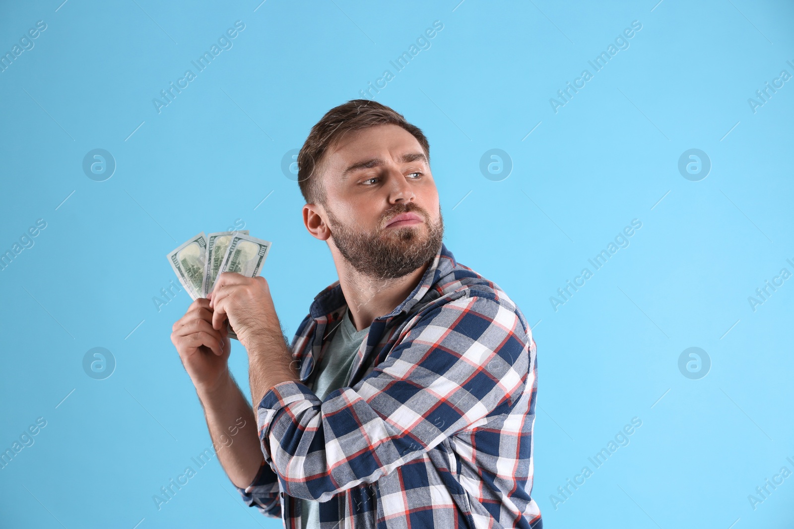 Photo of Greedy young man hiding money on light blue background