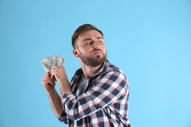 Photo of Greedy young man hiding money on light blue background