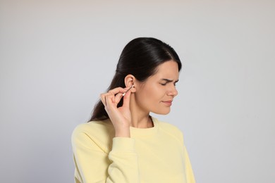 Photo of Young woman cleaning ear with cotton swab on light grey background