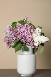 Photo of Beautiful lilac flowers in vase on wooden table against beige background