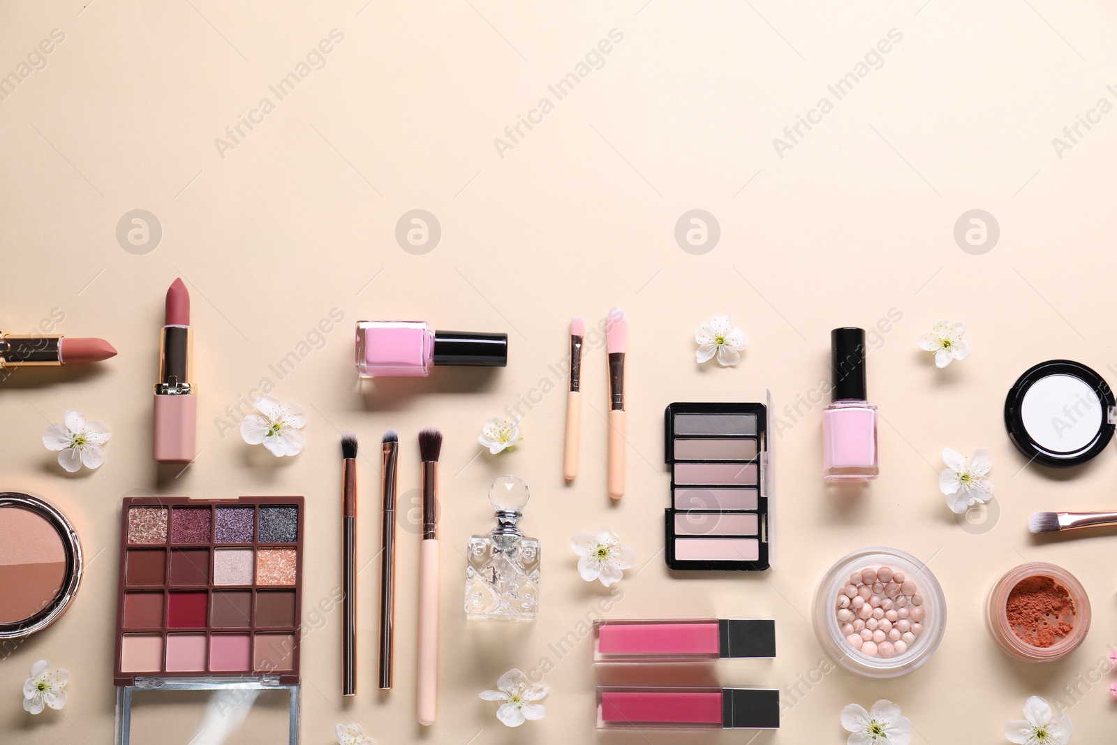 Photo of Flat lay composition with different makeup products and beautiful spring flowers on beige background, space for text