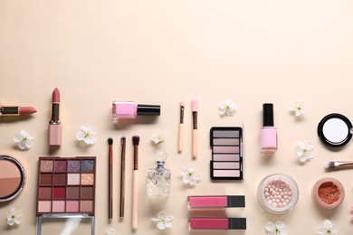 Flat lay composition with different makeup products and beautiful spring flowers on beige background, space for text