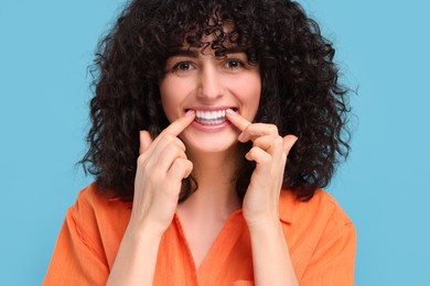 Young woman applying whitening strip on her teeth against light blue background