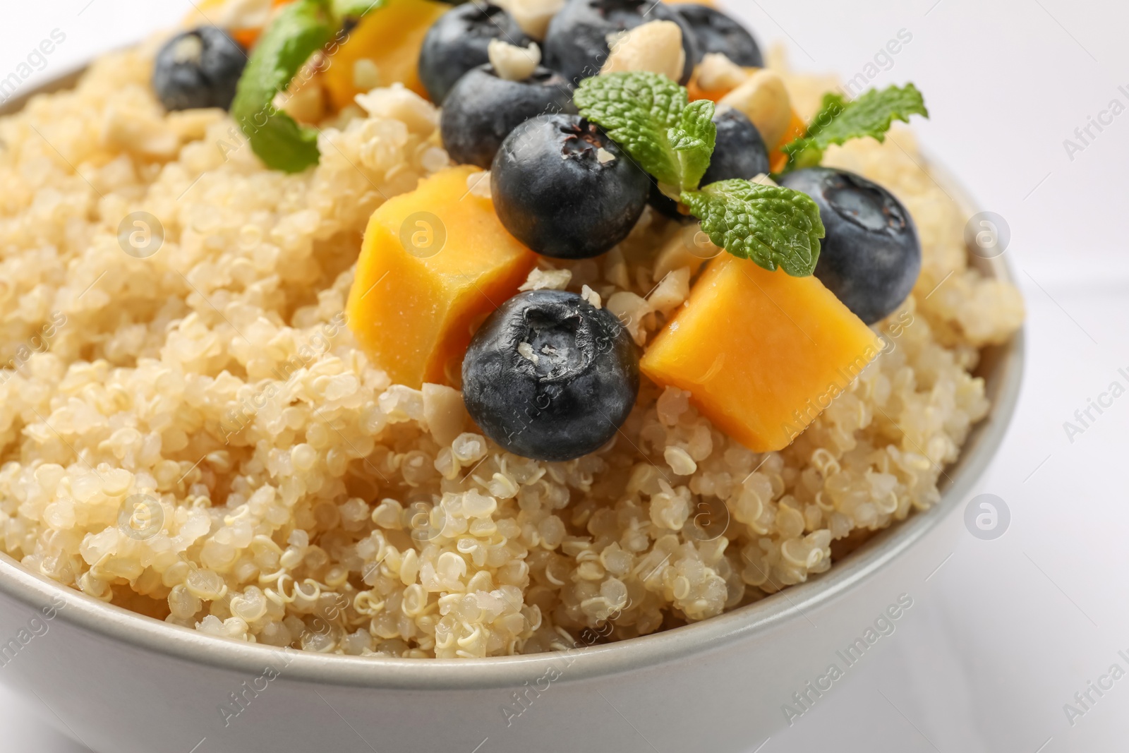 Photo of Tasty quinoa porridge with blueberries, pumpkin and mint in bowl on white table, closeup