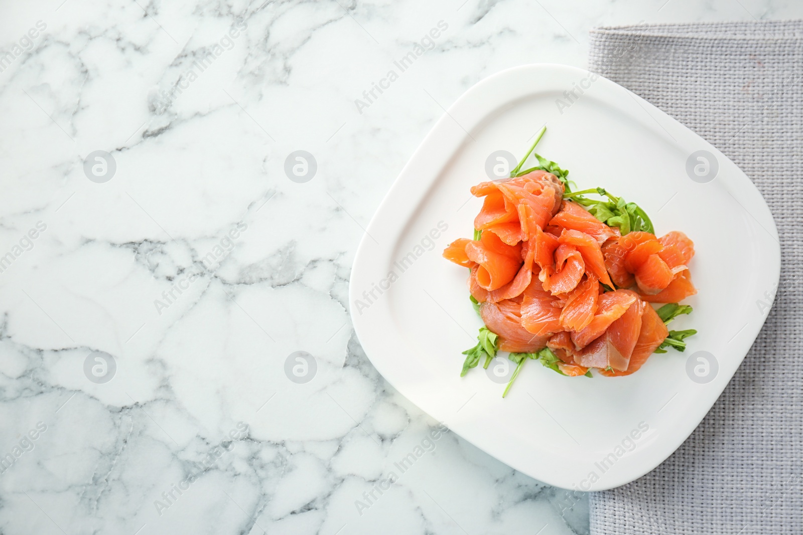 Photo of Plate with fresh sliced salmon fillet and arugula on marble background, top view