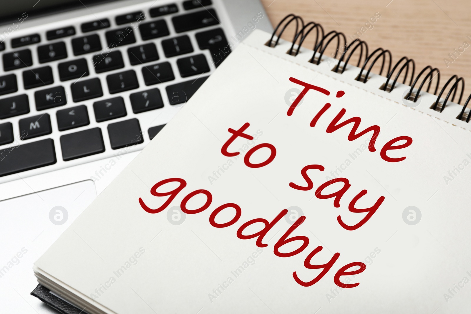 Image of Notebook with phrase Time to say goodbye and laptop on table, closeup