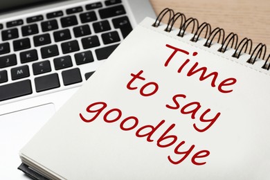 Image of Notebook with phrase Time to say goodbye and laptop on table, closeup