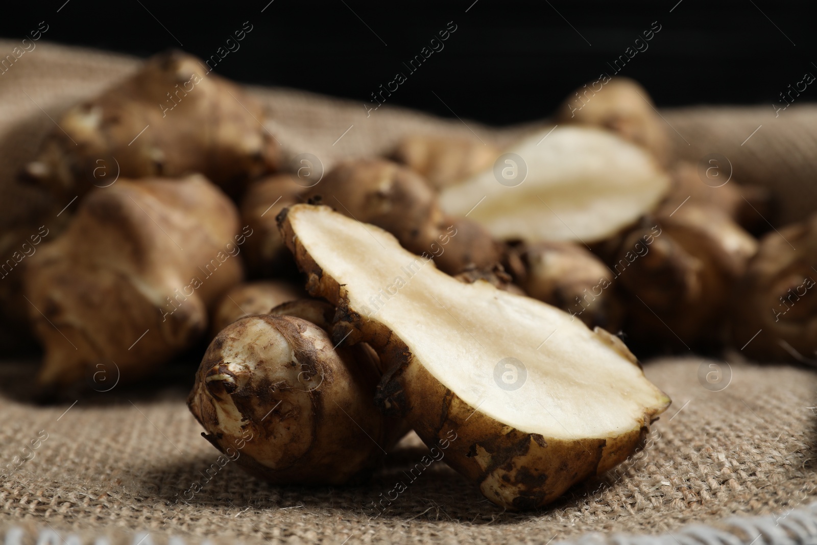 Photo of Jerusalem artichokes on bag against dark background, closeup