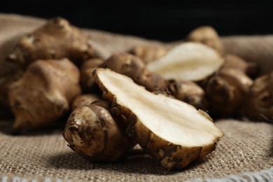 Photo of Jerusalem artichokes on bag against dark background, closeup