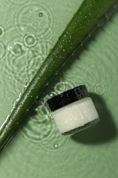 Photo of Jar of cosmetic product and aloe leaf in water on pale green background, flat lay