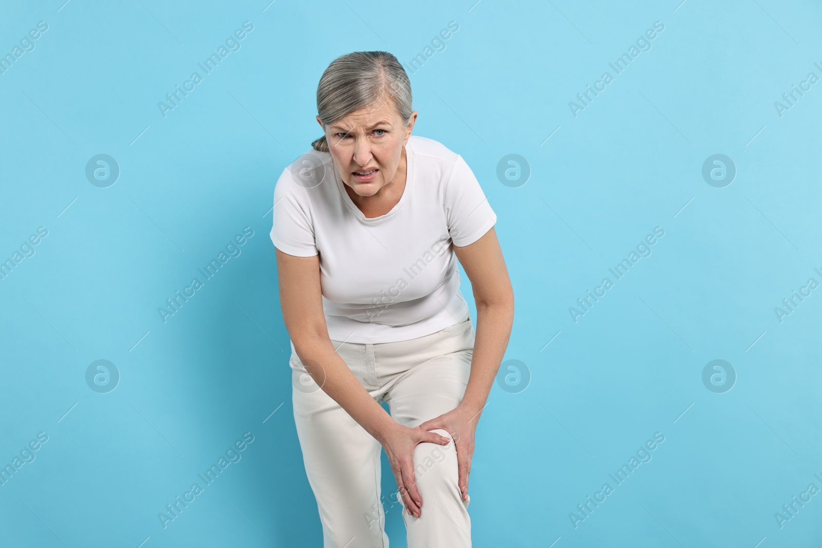 Photo of Arthritis symptoms. Woman suffering from pain in knee on light blue background