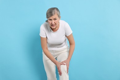 Photo of Arthritis symptoms. Woman suffering from pain in knee on light blue background