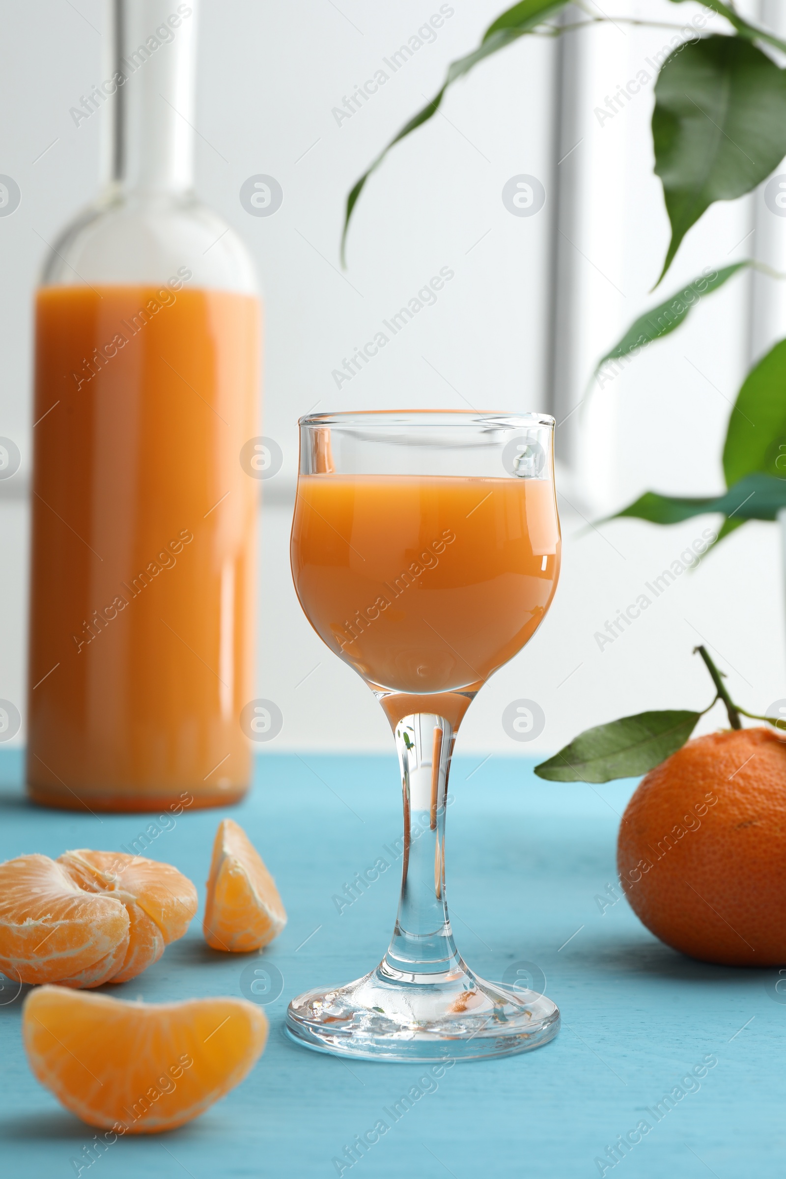 Photo of Delicious tangerine liqueur and fresh fruits on light blue wooden table