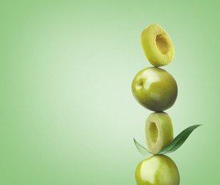 Cut and whole olives with leaf on light green background, space for text