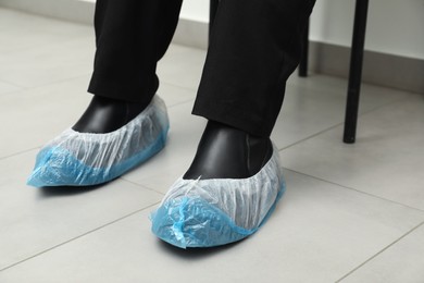 Photo of Woman wearing blue shoe covers onto her boots indoors, closeup