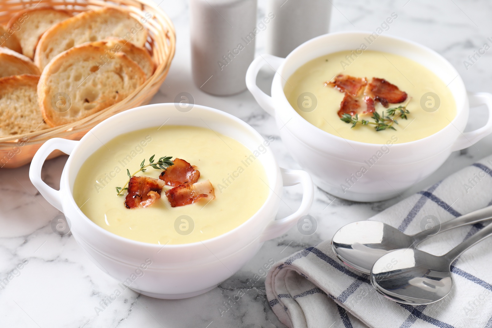 Photo of Tasty potato soup with bacon and rosemary in bowls served on white marble table