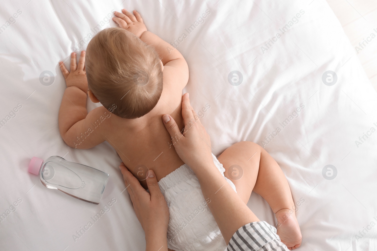 Photo of Mother massaging her cute baby with oil on bed, closeup