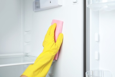 Woman cleaning empty refrigerator with rag, closeup